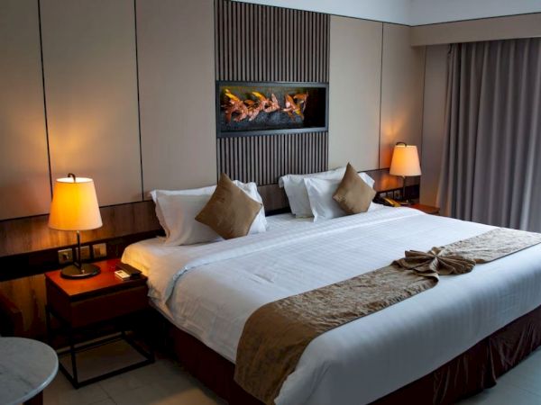 A cozy hotel room with a large bed, decorative pillows, warm lighting from lamps, and a window with curtains drawn to the side.