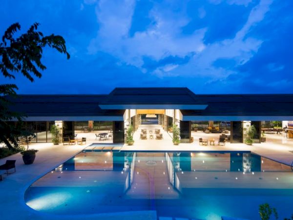 A modern building with a large illuminated pool at night under a blue sky.