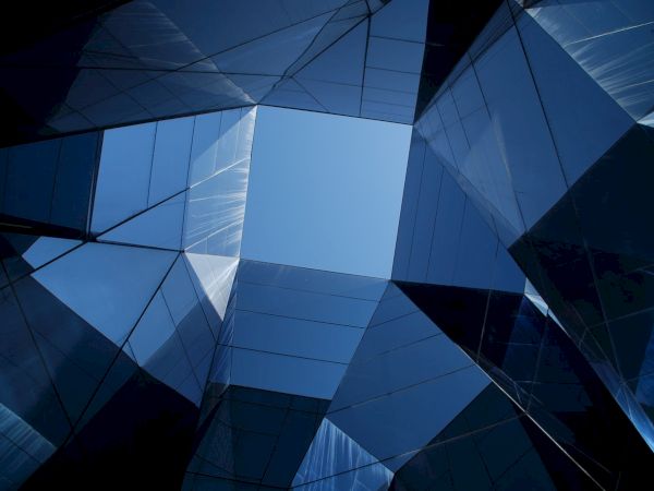 The image shows a modern building with reflective glass panels, forming a geometric pattern against a clear blue sky.