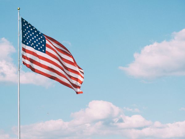 An American flag waves against a blue sky with a few clouds.