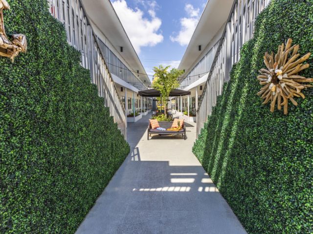 A courtyard with a pathway between two buildings, surrounded by greenery and seating areas.