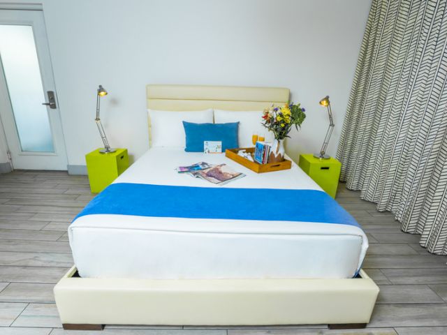 A neatly made bed with a blue and white comforter, two green nightstands, and a tray with flowers and magazines on it.