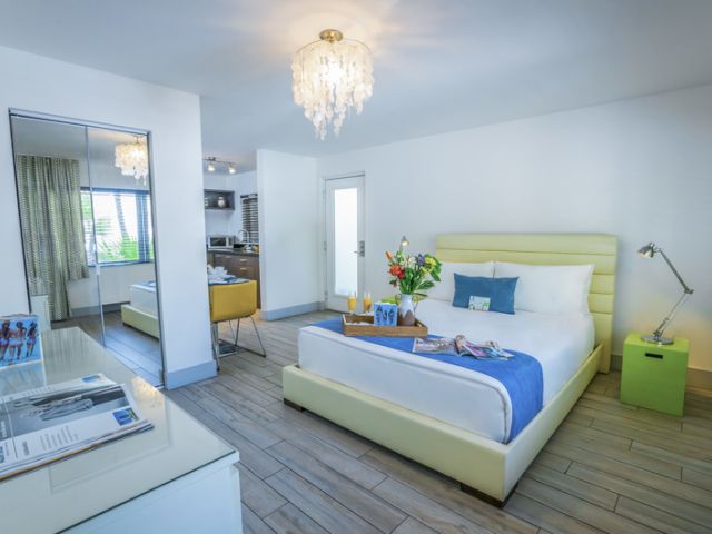 A wide view of a hotel suite with a king-sized bed, a kitchenette, and a chandelier.