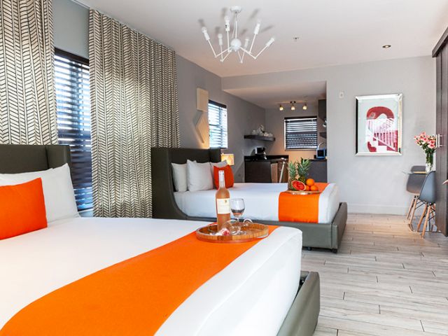 A wide view of a hotel suite with two beds, a sofa bed, and a kitchenette.
