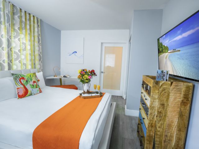 A hotel room with a bed, TV, flowers, and artwork.