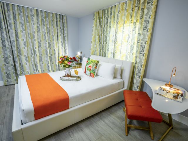 A hotel room with a bed, desk, chair, and curtains