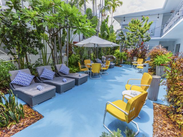 A small outdoor seating area with blue flooring, yellow chairs, gray lounge chairs, and umbrellas.