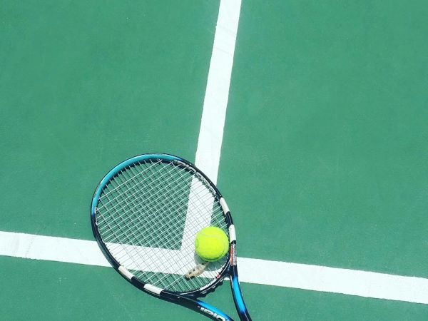 A tennis racket and ball on a green court surface with white lines intersecting.