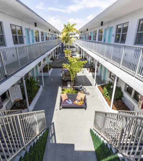 Aerial view of a hotel courtyard with a seating area, palm tree, and balconies on both sides.