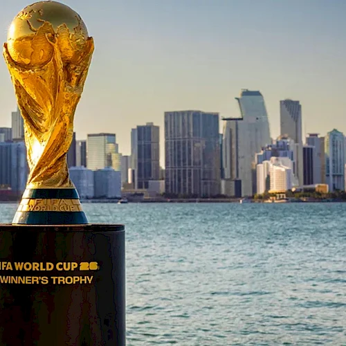 A FIFA World Cup Winners&rsquo; Trophy sits on a pedestal by the water with a city skyline in the background.